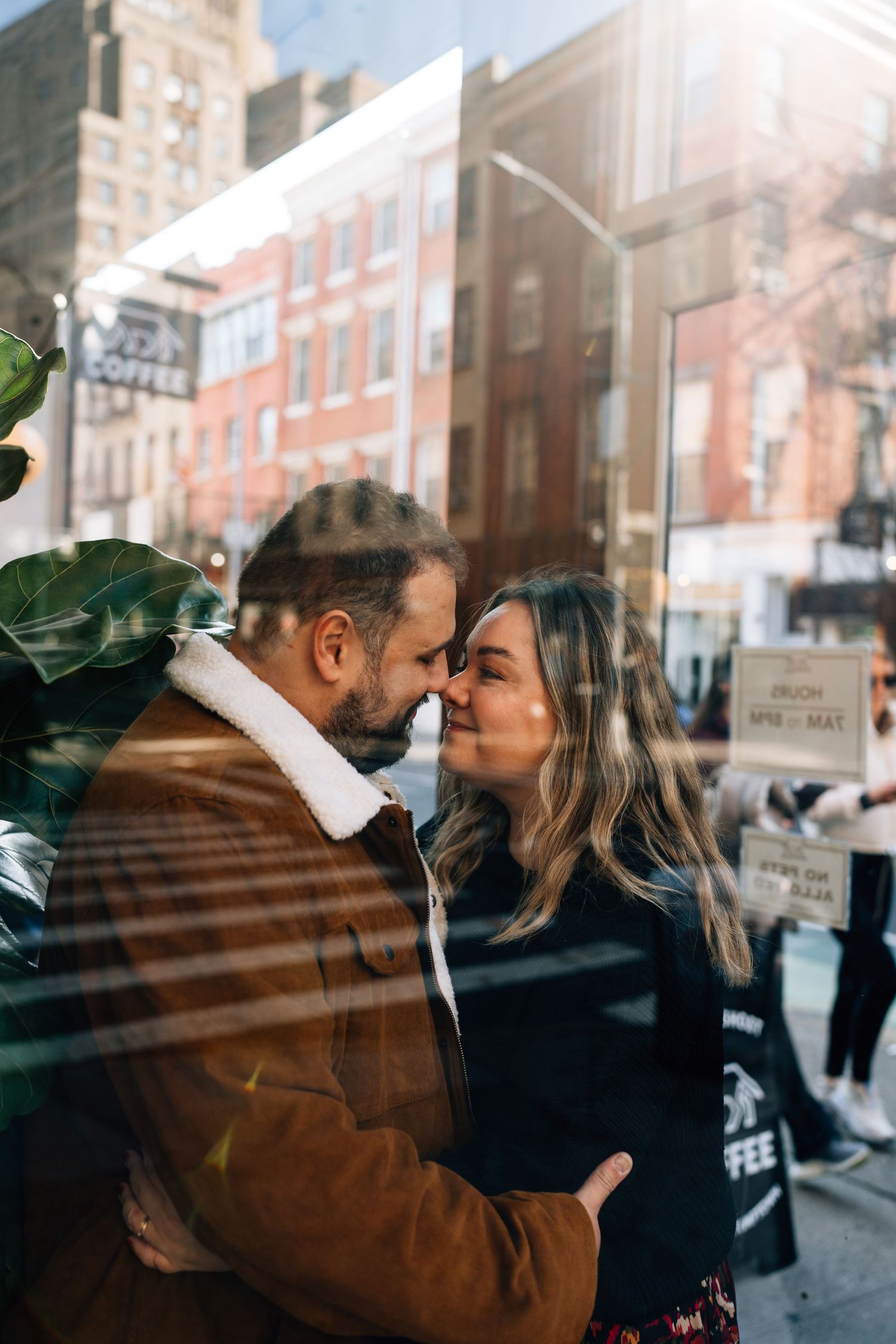 Couple sharing intimate moment through reflective window in city setting.