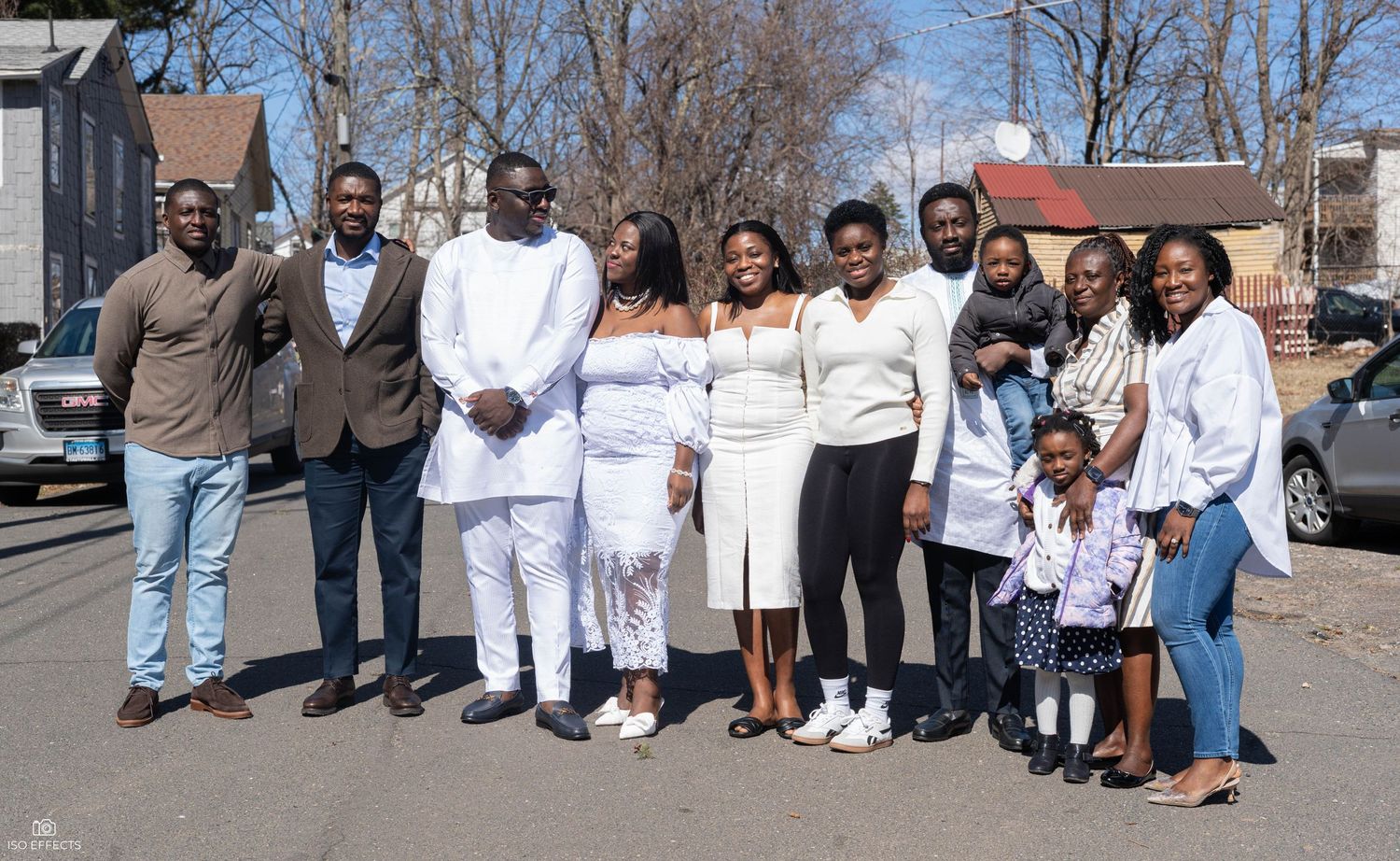 A group of people dressed in white and casual attire pose together for a group photo outdoors on a sunny day.