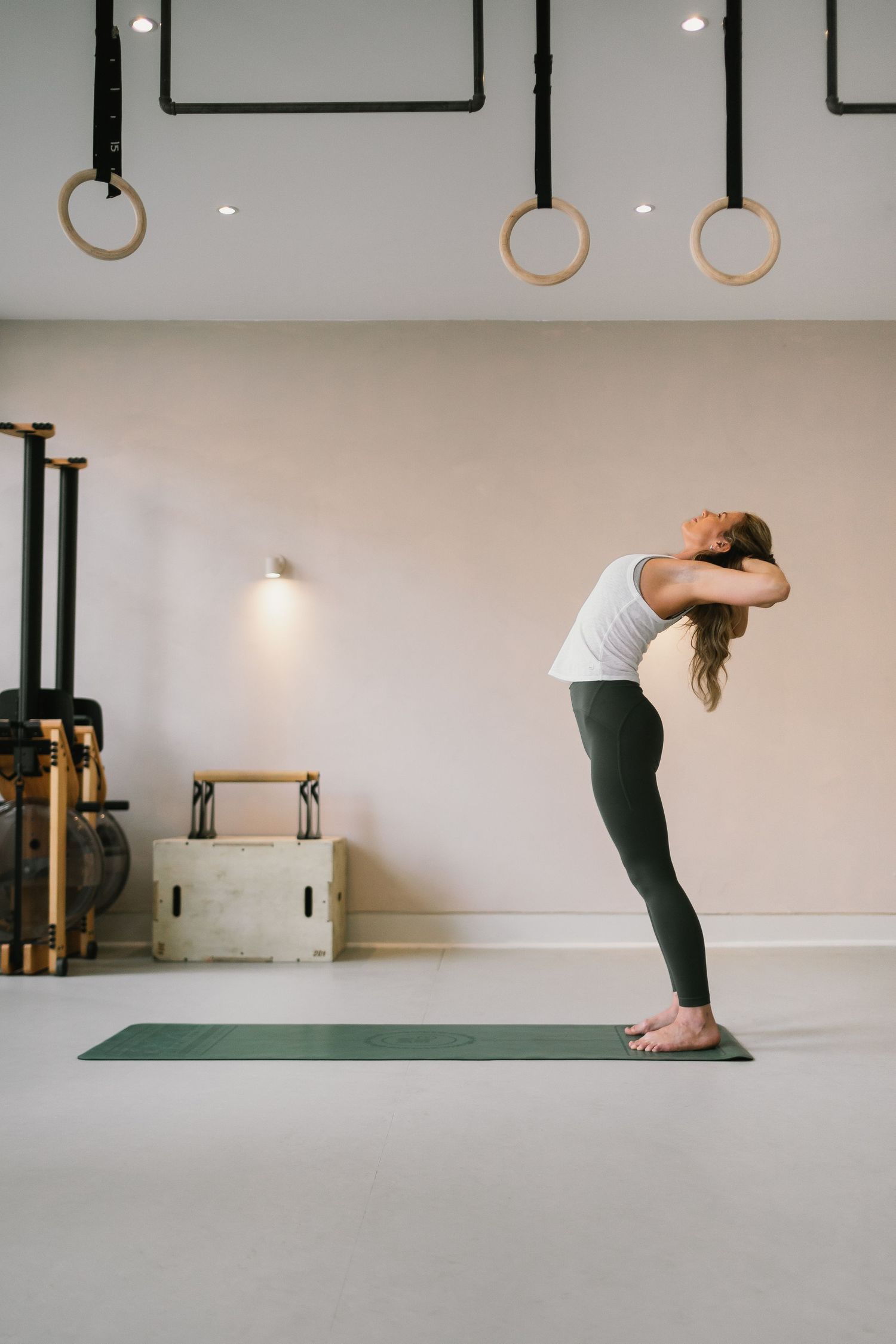 Three photos showing yoga practice progression from standing forward bend to uttanasana pose on a green mat in a studio.
