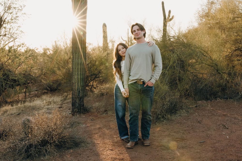A couple walks along a desert trail surrounded by saguaro cacti and desert vegetation at golden hour in Phoenix Arizona.
