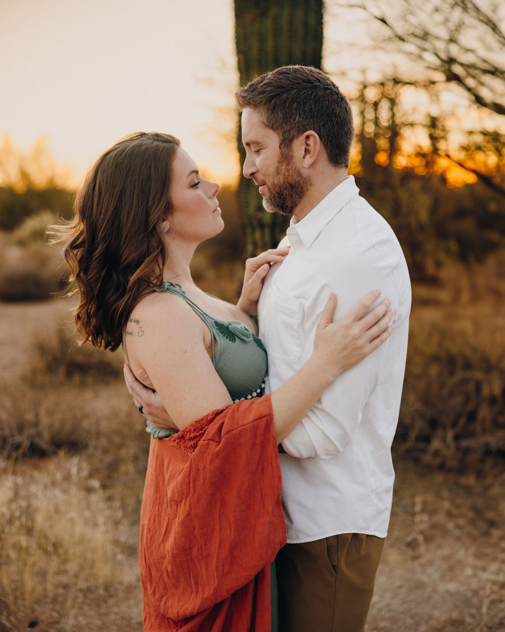A couple gazing into each others eyes as the sun slowly sets in the background.