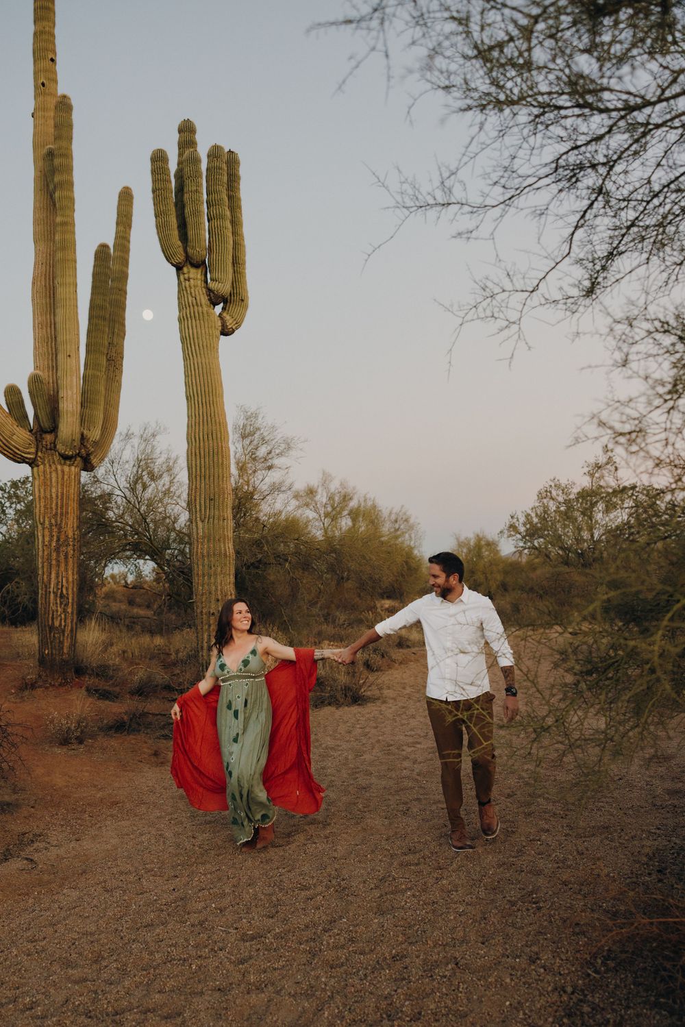 A couple dances together among tall saguaro cacti in a desert landscape at dusk In Phoenix Arizona.