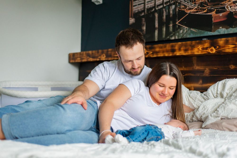 A couple in white t-shirts and jeans lounges together on a bed with rustic wooden headboard.