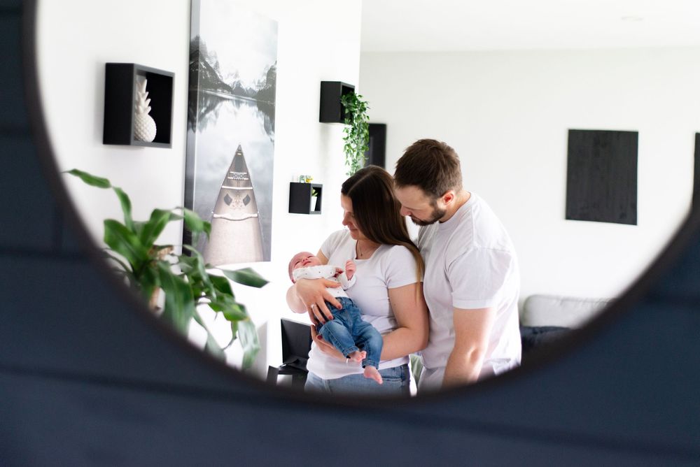 Mirror reflection captures tender family moment with baby in modern home interior.