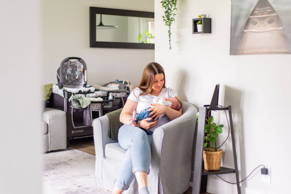A person sits in a cozy gray armchair nursing an infant in a modern living room setting.