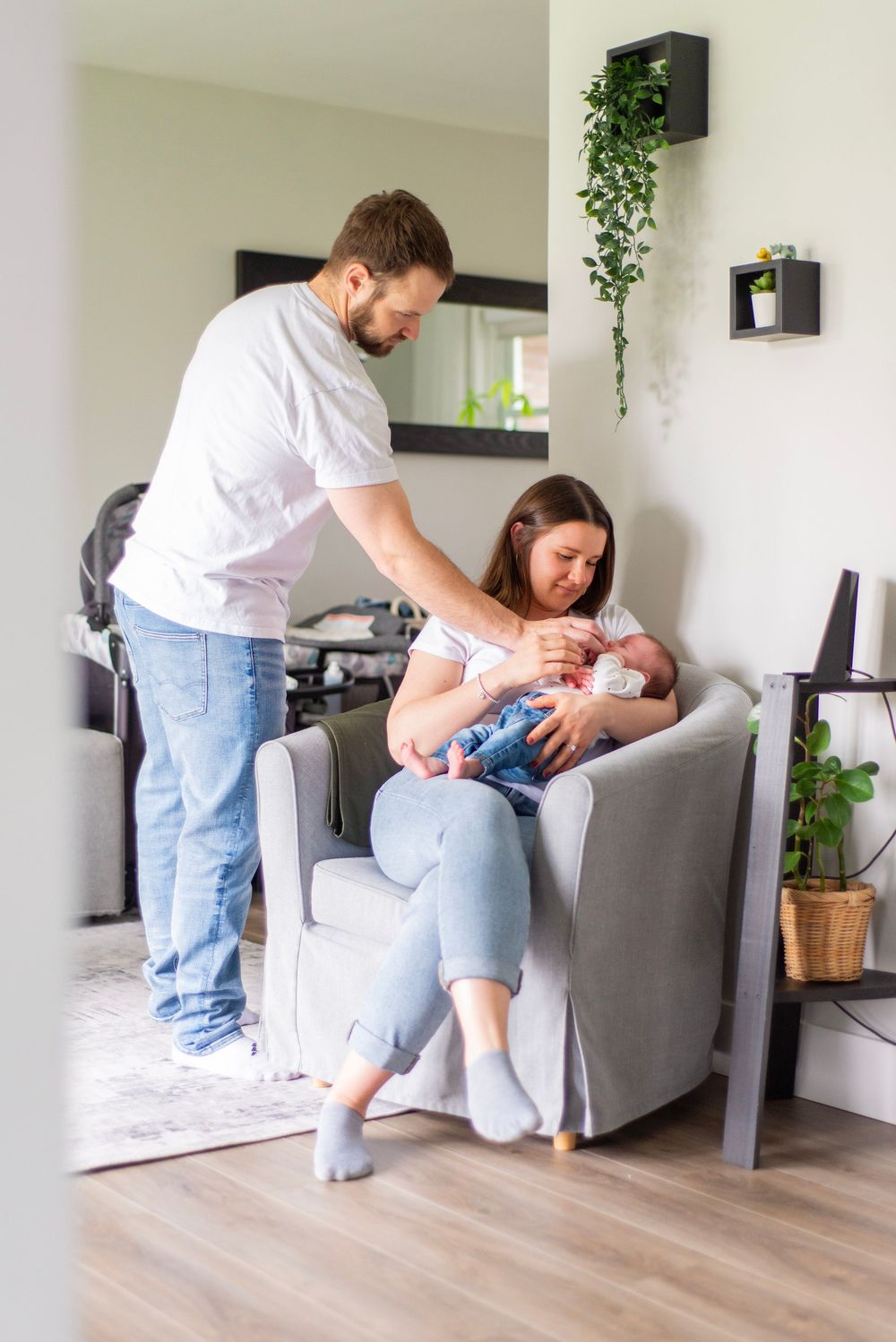 Parents care for newborn baby in modern living room with hanging plants.