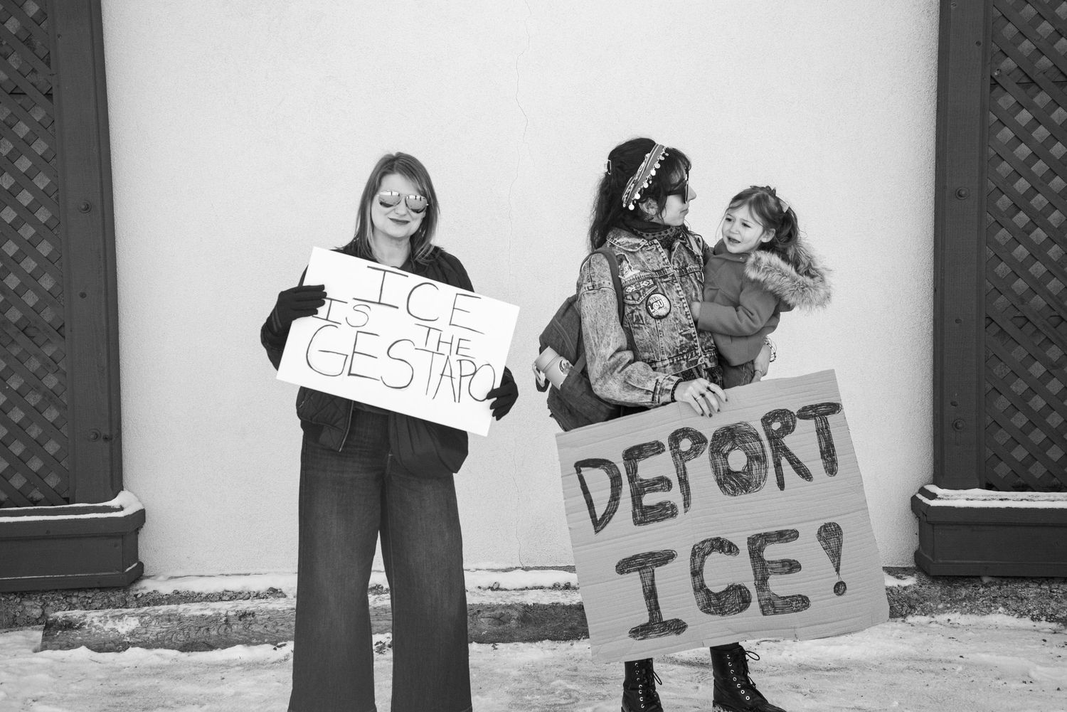 Black and white photo of two women holding ICE protest signs outdoors in winter.