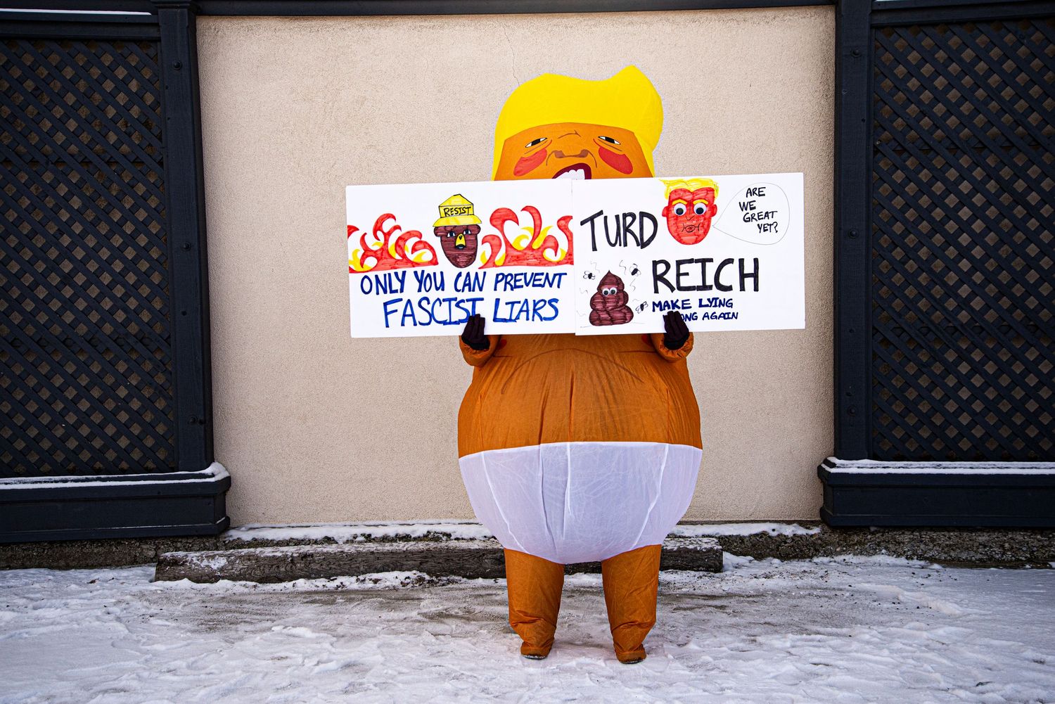 Person in inflatable Trump baby costume holding anti-fascist protest sign in snow.