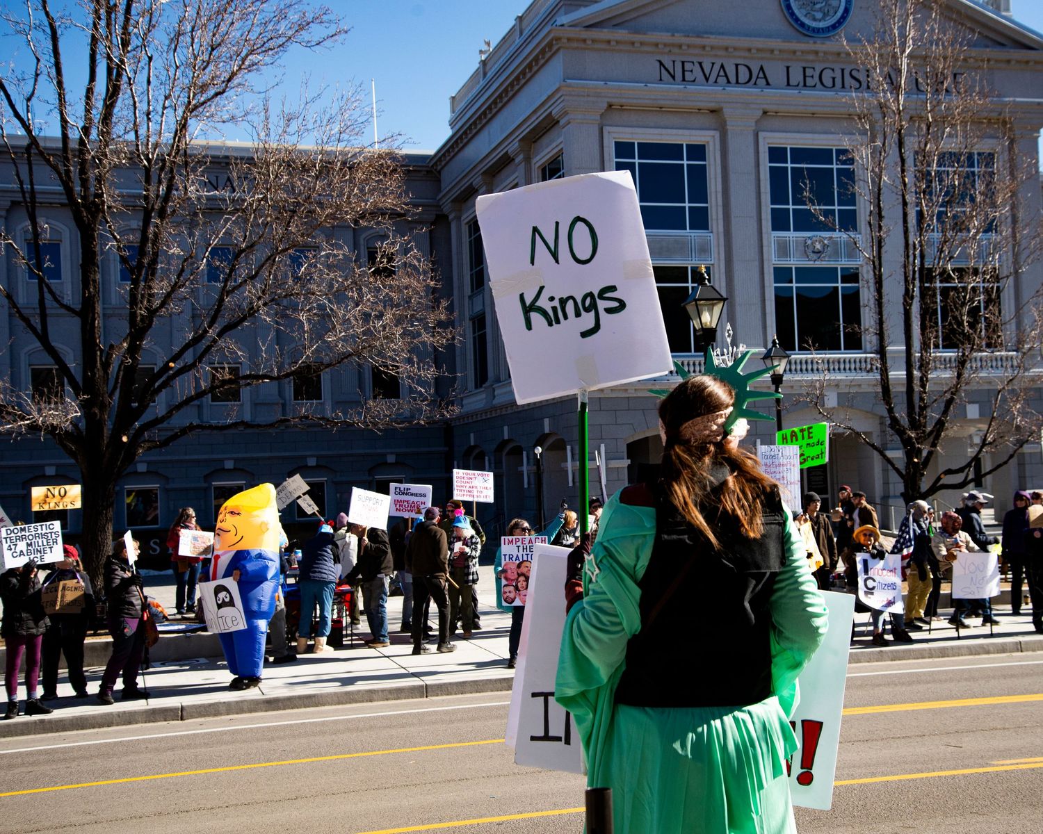 Woman in green costume holds No Kings sign at protest outside Nevada Legislature building.