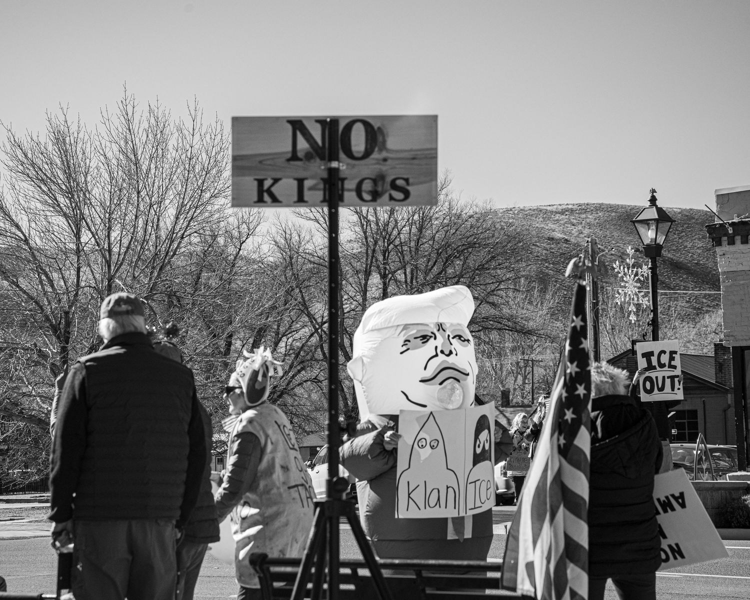 Protesters hold No Kings sign and Trump caricature balloon at outdoor political rally in black and white.