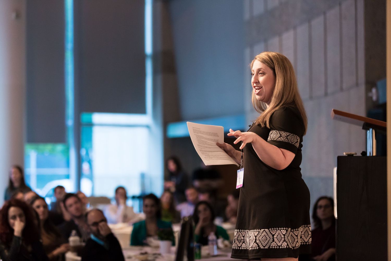 Speaker presenting to an audience at a business conference from behind a podium in a modern meeting space.