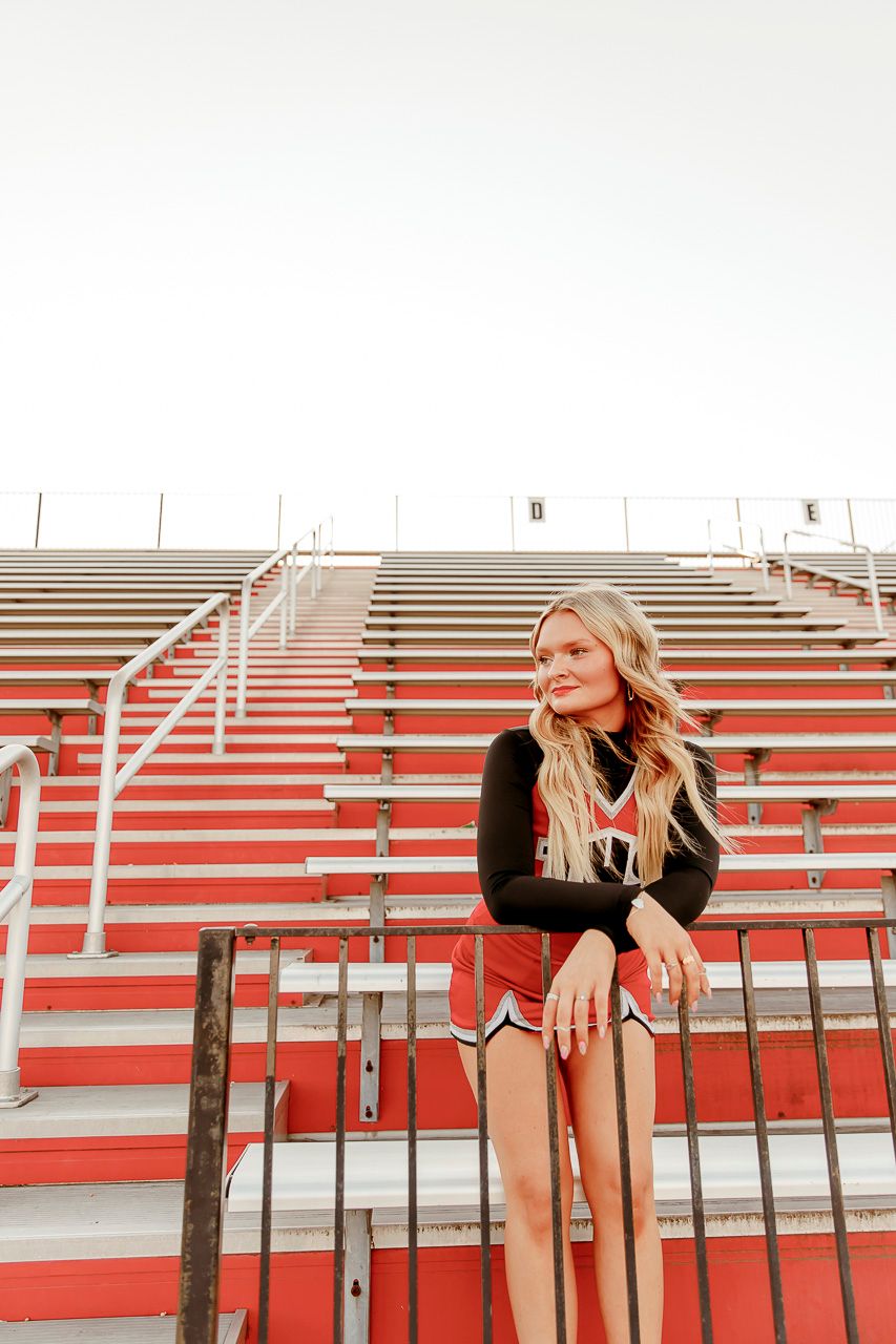 Person in black long-sleeve top sits on bright red stadium bleachers with white railings during golden hour.