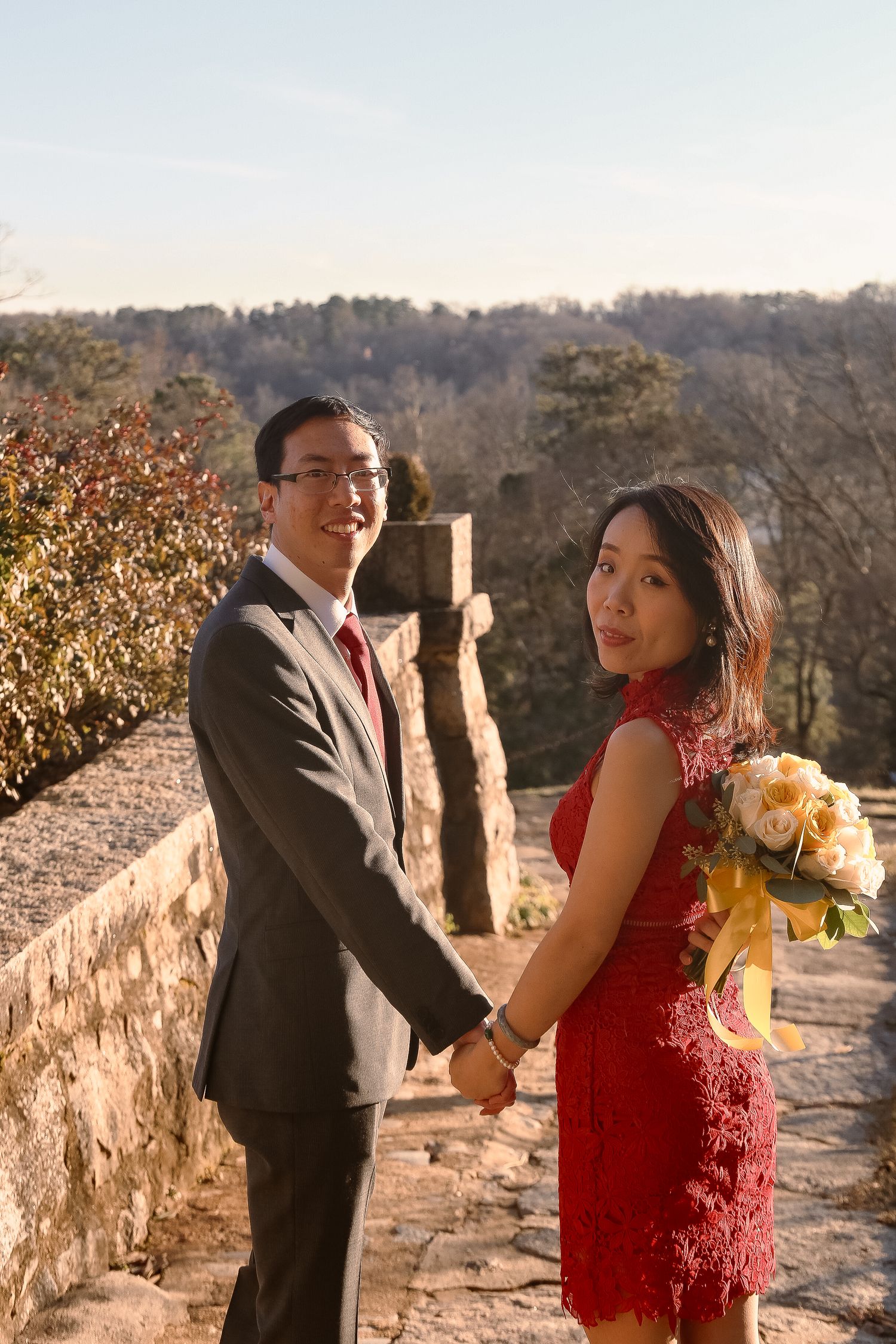 Couple in formal attire poses on stone path during outdoor photoshoot.
