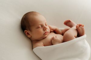 Sweet newborn baby sleeping peacefully wrapped in white blanket.