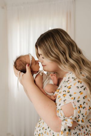 Tender moment with baby wearing white onesie against light background.