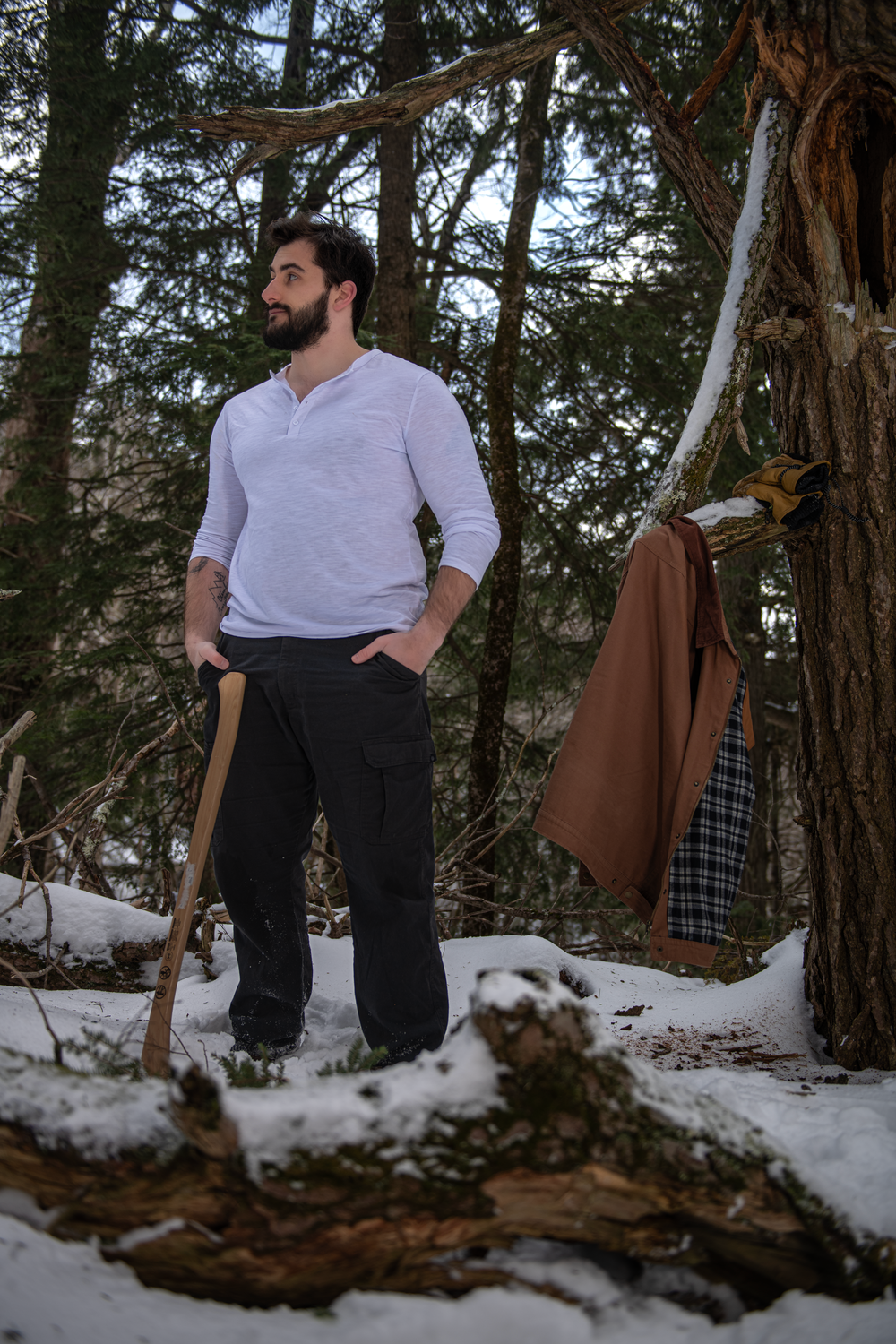 Winter woodland scene with a lilac sweater and brown coat hanging on a tree branch in snowy surroundings.