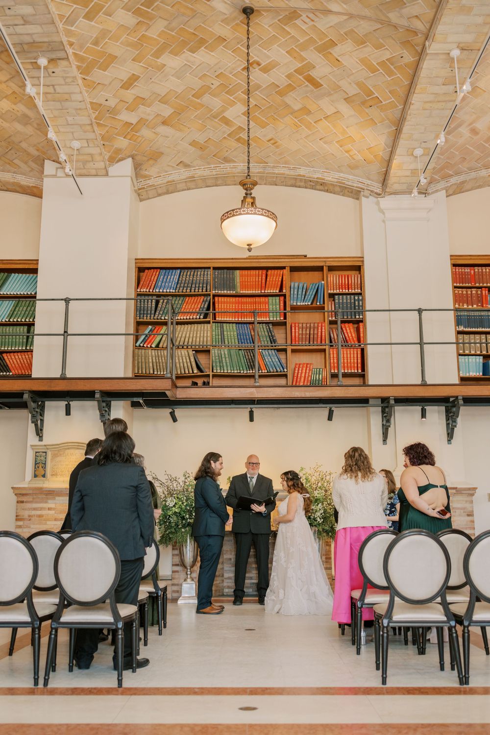Library wedding ceremony setup with vintage bookshelves and elegant pendant lighting.