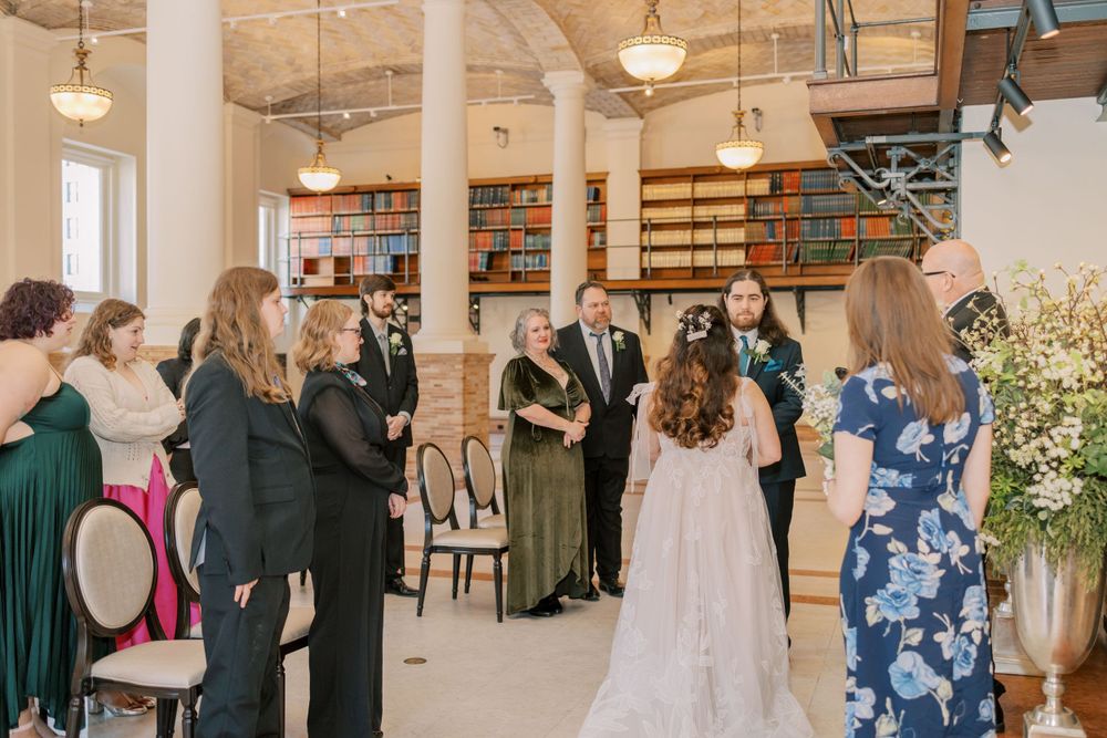 Wedding ceremony in a library venue with guests watching as vows are exchanged.