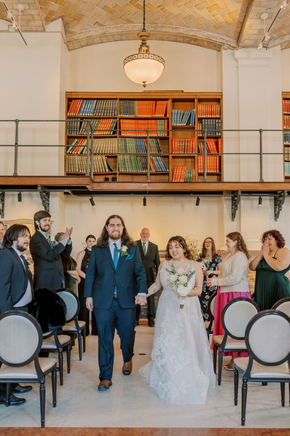 Wedding recessional in a beautiful library venue with vintage bookshelves and pendant lighting.