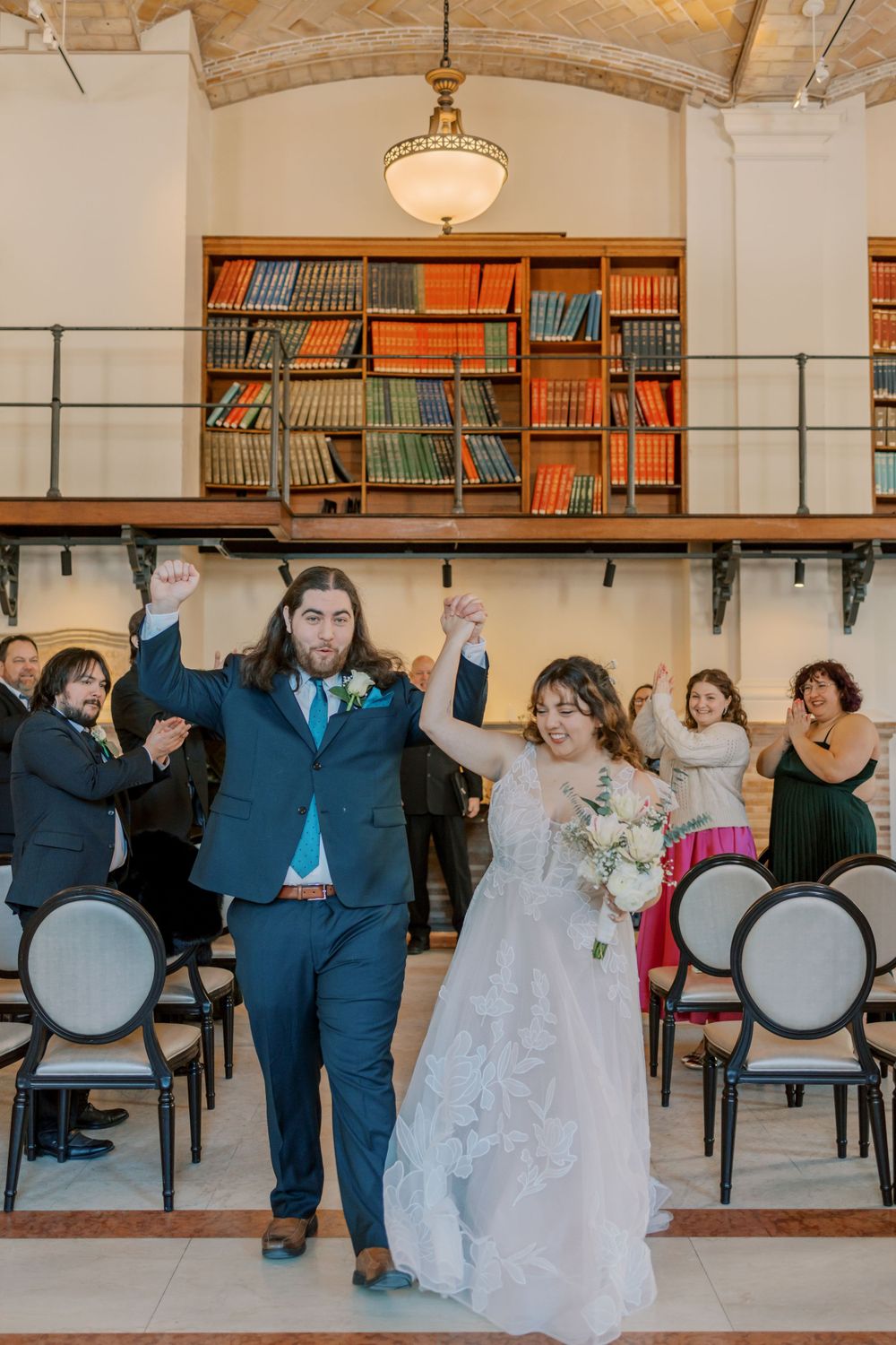 Newlyweds celebrate with raised arms during their library wedding ceremony.