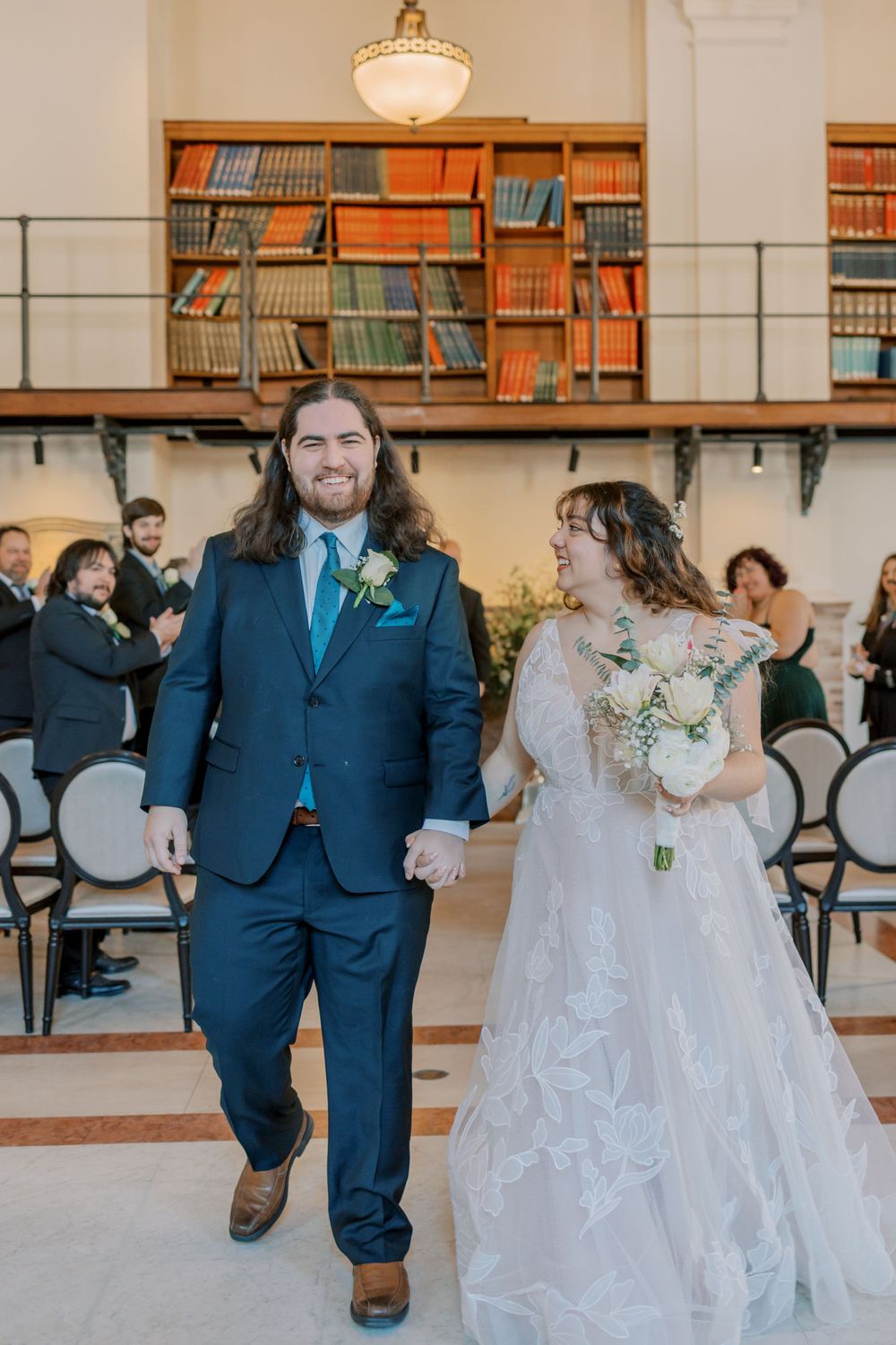 Wedding couple walks down aisle in elegant library venue with vintage book collection backdrop.