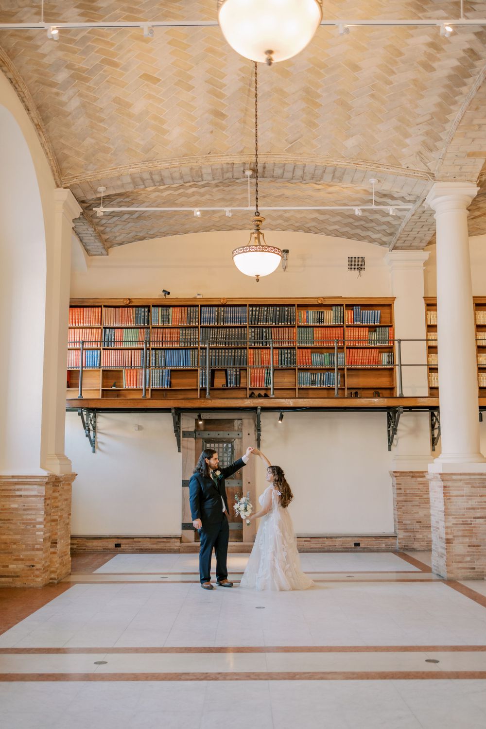 Romantic wedding moment beneath arched ceiling and library bookshelves.
