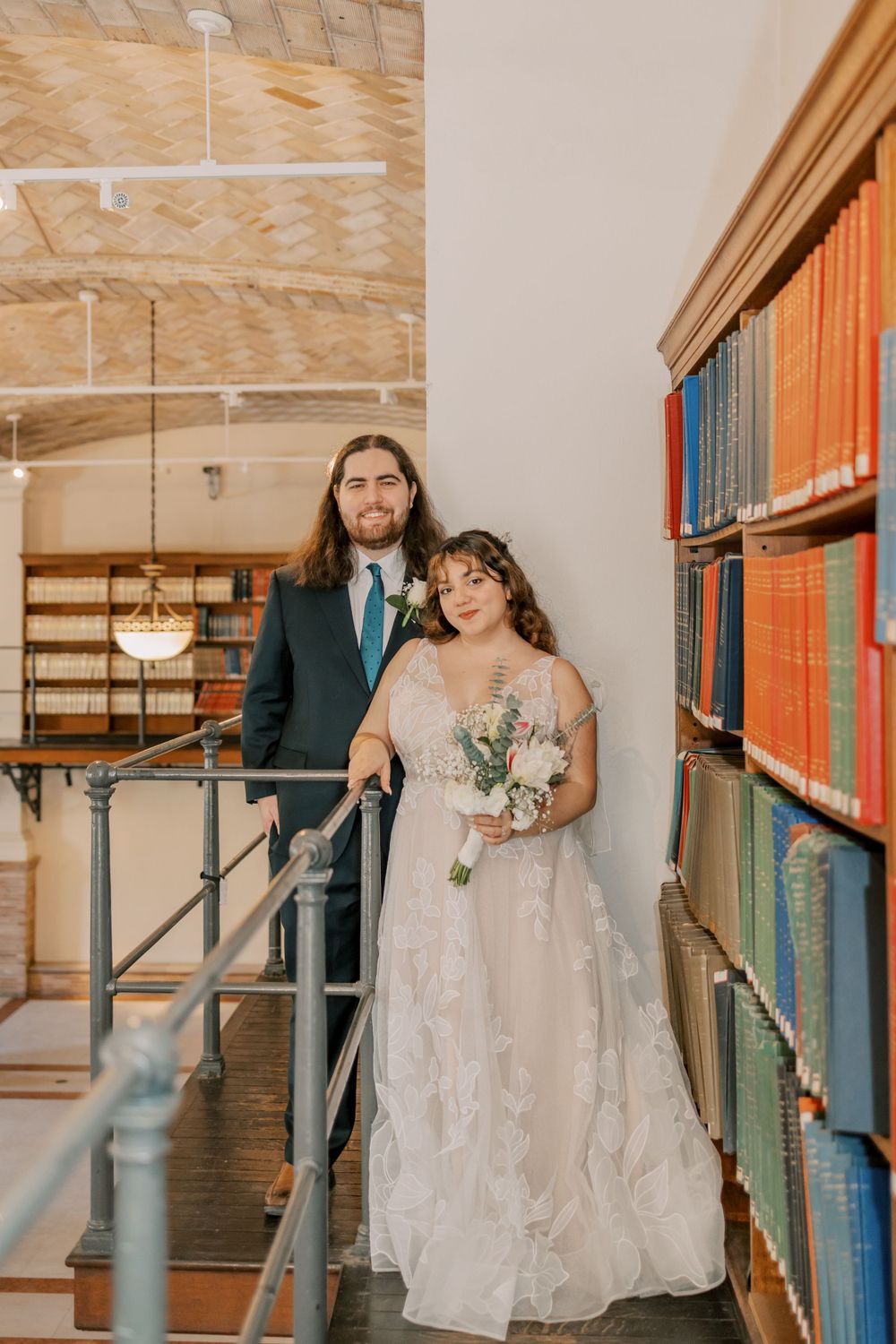 A romantic wedding photoshoot in a library featuring a couple surrounded by vintage books and wooden shelving.