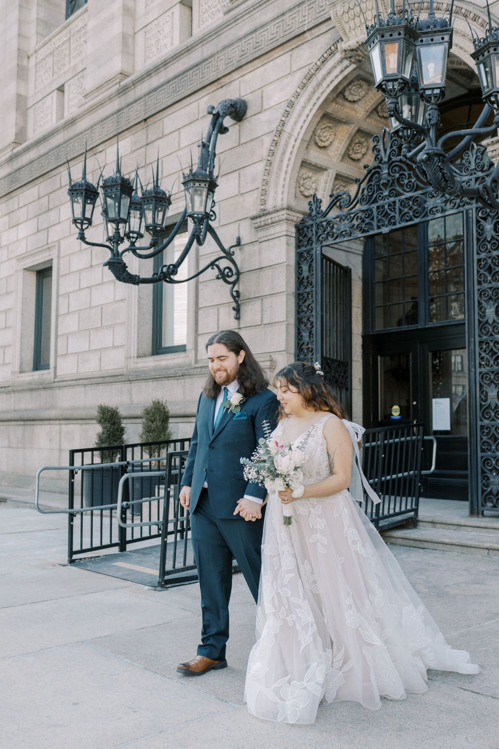 A wedding couple poses outside a grand building with ornate iron lampposts and architectural details.