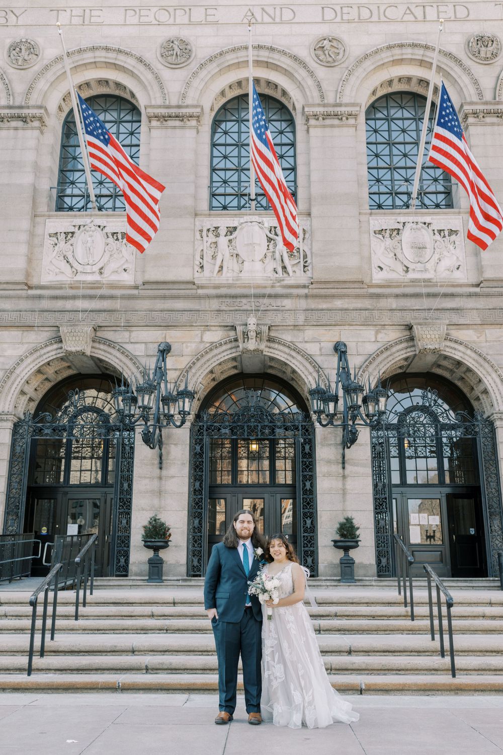 A wedding portrait in front of a historic building with American flags and classical architecture.
