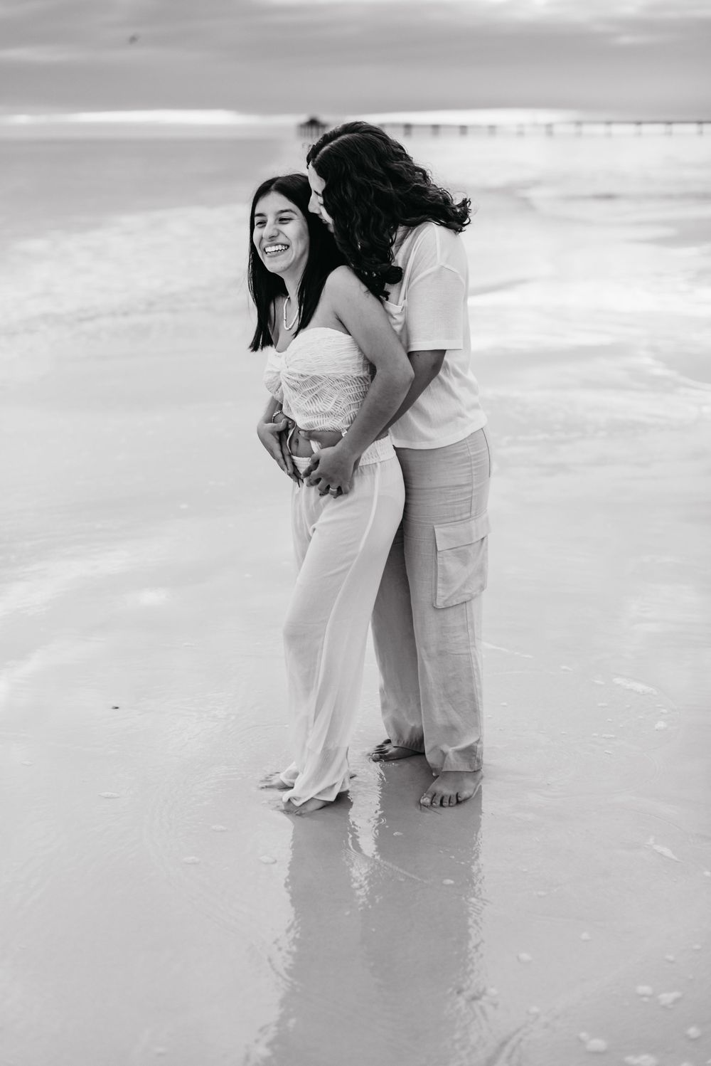 Couple in light colored clothing embracing on white sandy beach in monochrome.