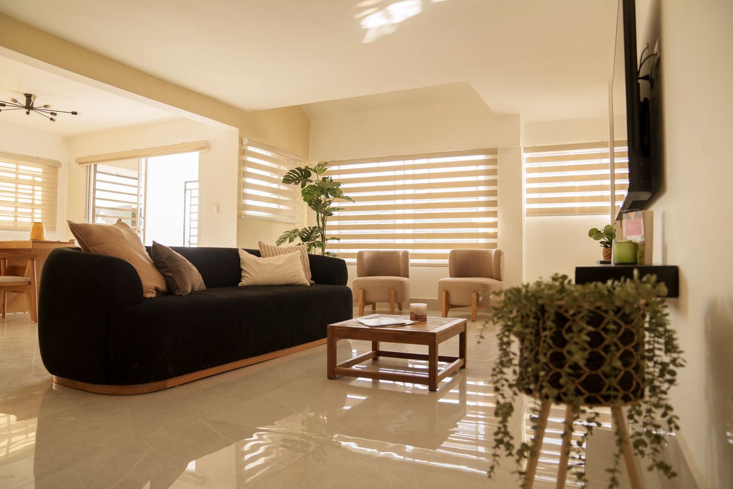 Modern living room with natural light streaming through horizontal blinds and sleek black furniture.