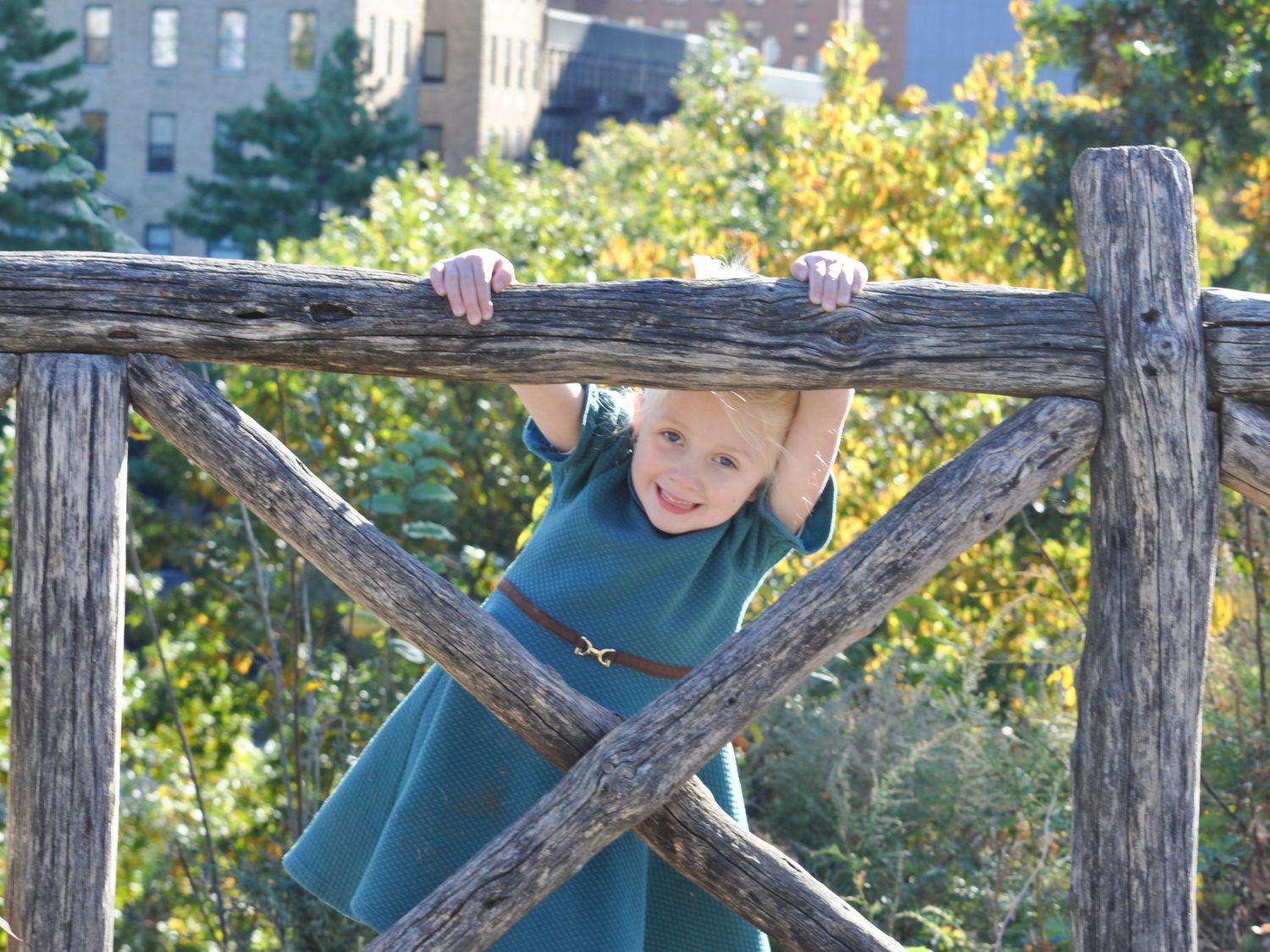 A young girl peeks through a rustic fence in Central Park, NYC, with a playful and curious expression.