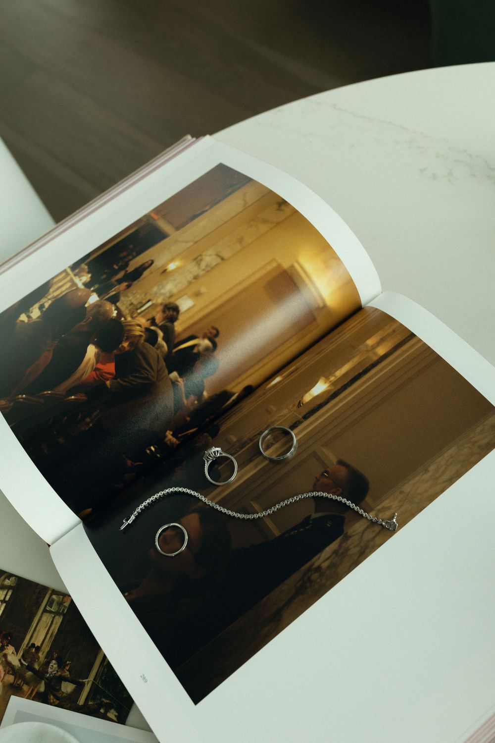 A page in a photo album showing wedding rings arranged in an artistic composition with blurred guests in background.