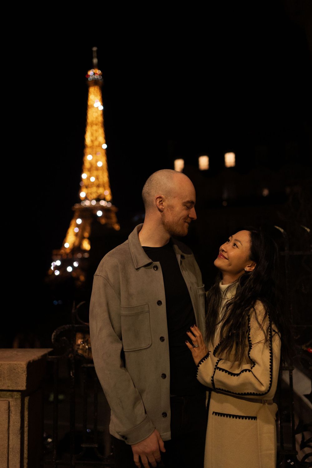 A couple shares a romantic moment at night with the illuminated Eiffel Tower glowing in the background.