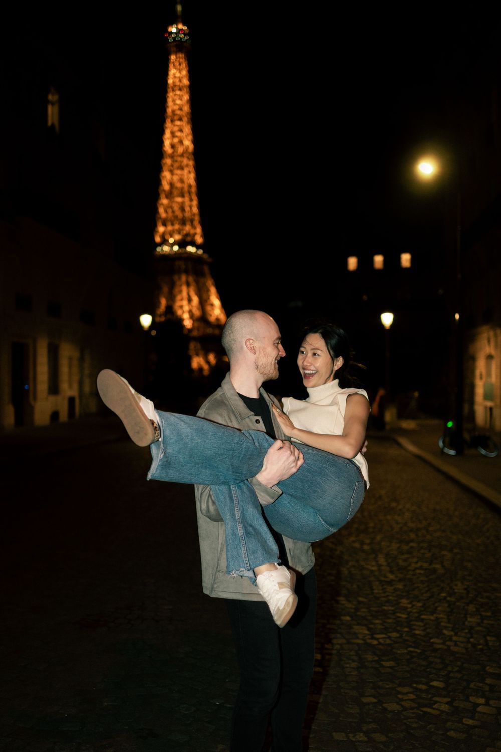 A romantic couple shares an intimate moment at night with the illuminated Eiffel Tower glowing in the background.