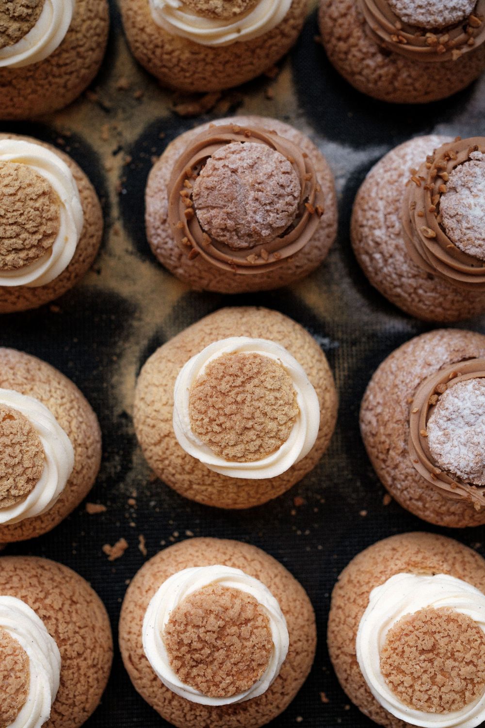 Chocolate cookies with cream centers arranged on a dark surface in rows.