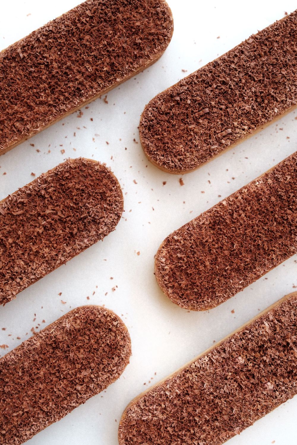 Chocolate covered ladyfinger cookies arranged in diagonal rows on white background.