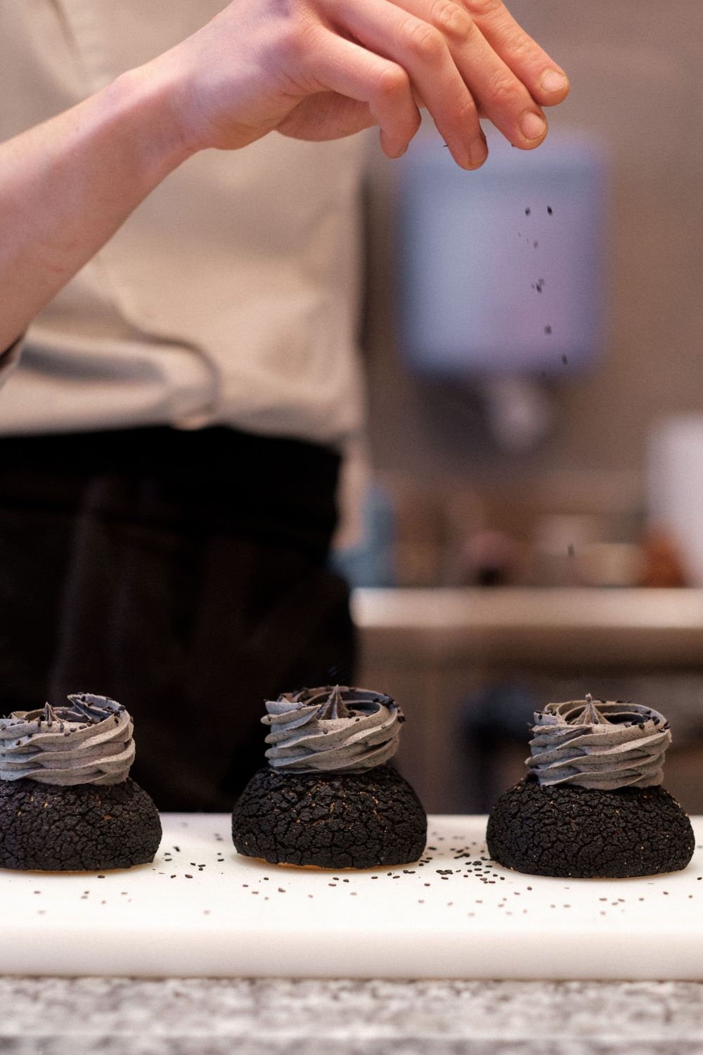 Three chocolate cupcakes with gray frosting being garnished on a white serving plate.