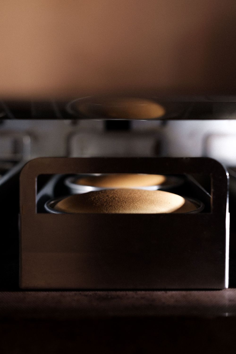 A golden circular baking pan illuminated in a dark professional kitchen setting.