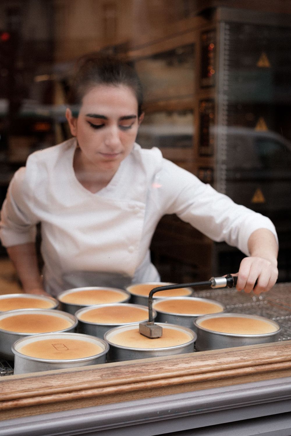 A pastry chef preparing multiple round desserts in metal molds in a professional kitchen.