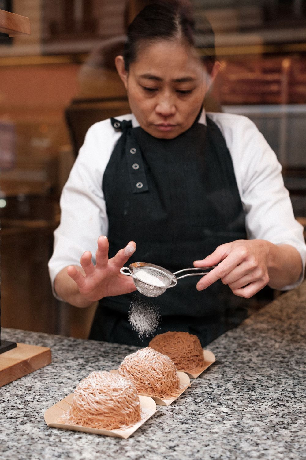 A chef dusting powdered sugar over chocolate desserts arranged on parchment squares.
