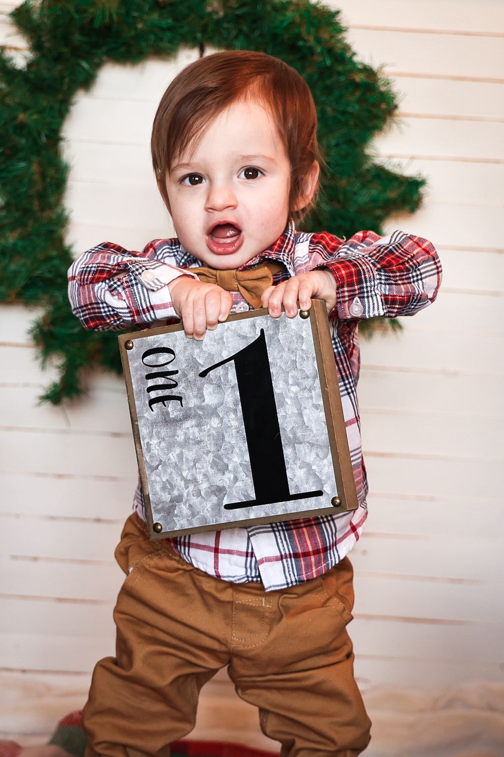 Holiday themed photo with plaid shirt and metal number one sign against wreath background.