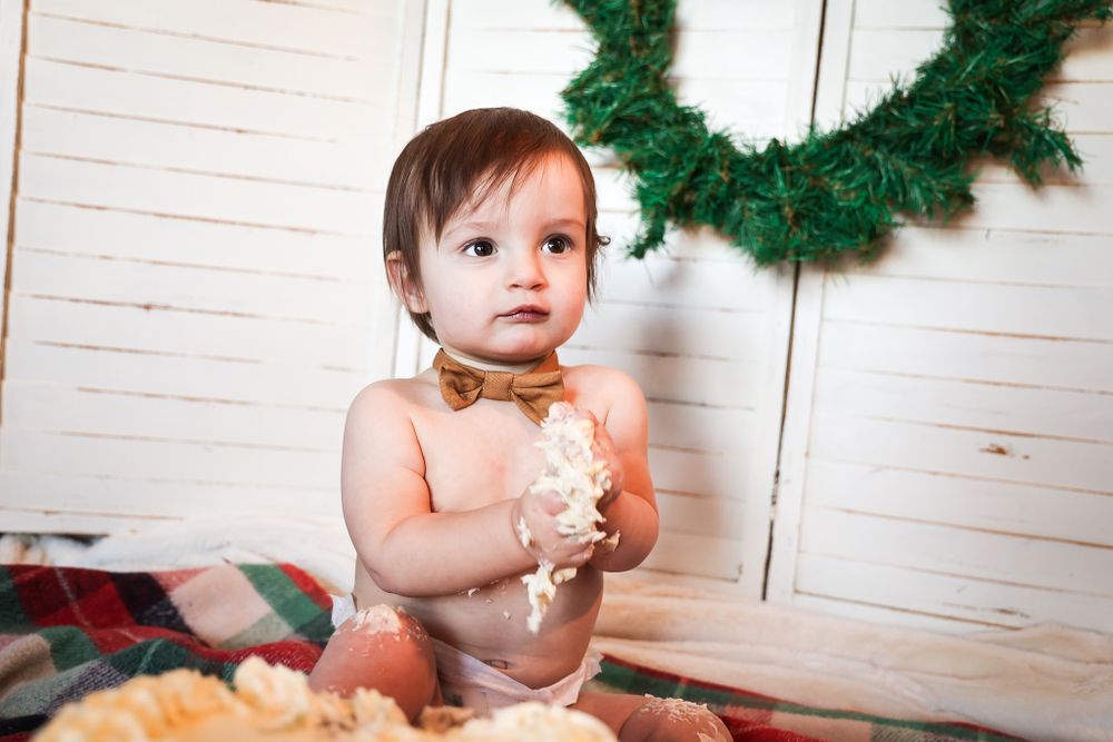 Holiday cake smash photoshoot setup with white walls and green wreath decoration.