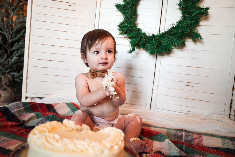 Candid moment during cake smash photoshoot with holiday decorations and plaid blanket.