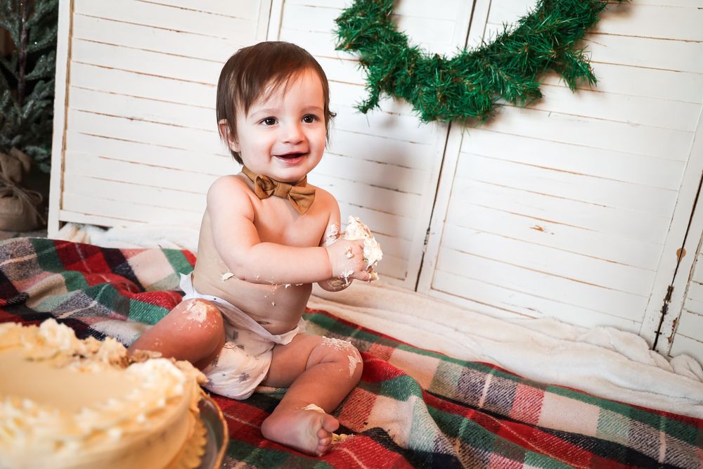 Joyful cake smash photography session with holiday greenery and plaid backdrop.