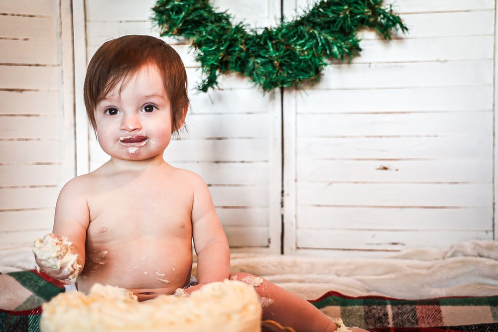 First birthday cake smash session with white shiplap walls and festive wreath.