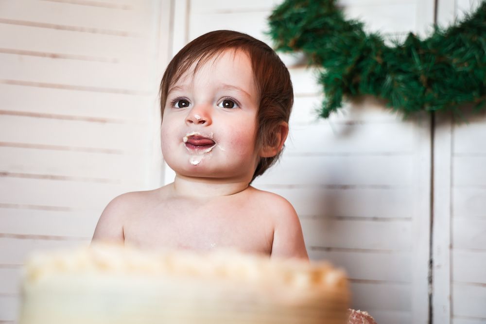 A small child wearing nothing but a smile sits in front of a holiday wreath decoration.