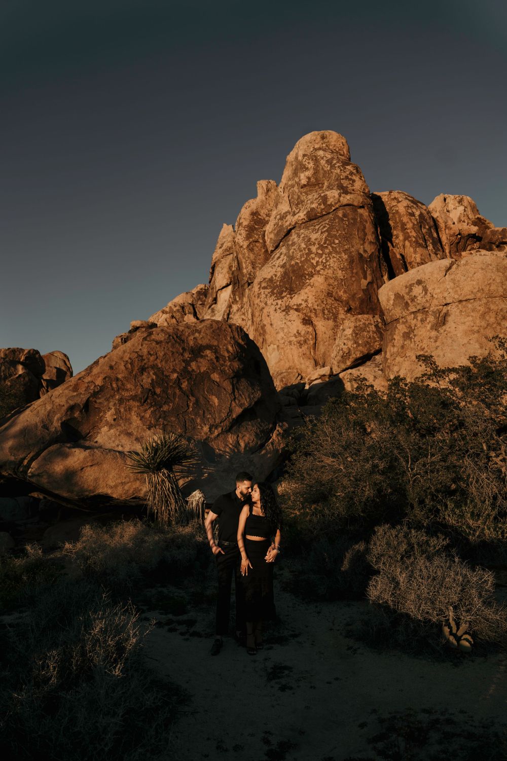 Silhouette of hikers standing amidst desert rocks at golden hour with dramatic light illuminating rugged rock formations.