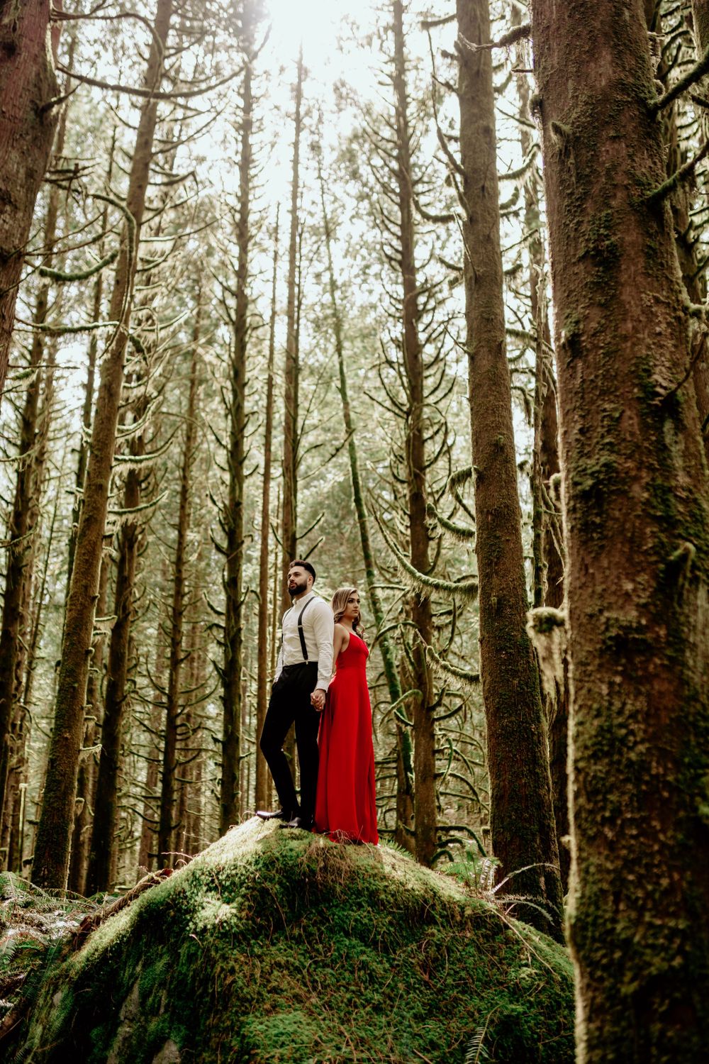 A couple standing on a mossy boulder in a misty evergreen forest with tall trees in the Pacific Northwest.
