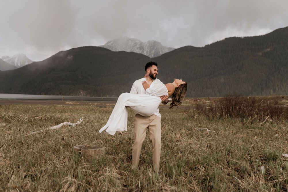 A romantic wedding couple embraces in a mountain meadow with misty peaks in the background on an autumn day.